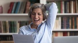 Excited cheerful senior business lady reading document at workplace with laptop
