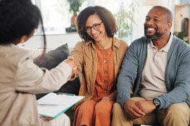 A mature couple on sofa shaking hands with a DFPI Consumer Services Officer